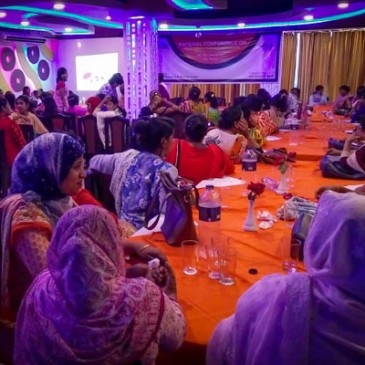 Participants at the conference sit a tables in brightly coloured venue with orange table cloths and purple lights